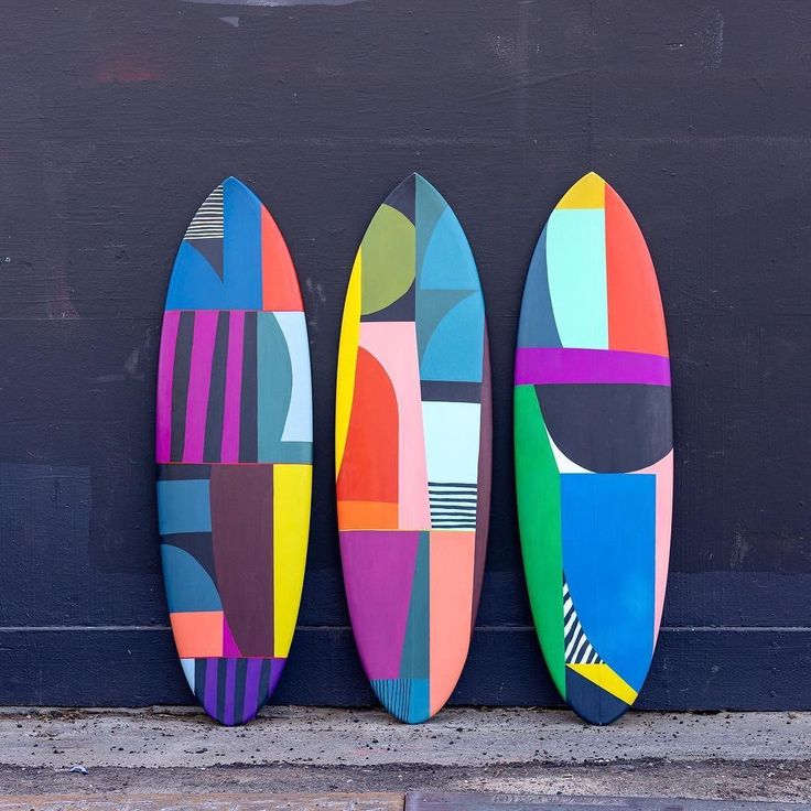 three colorful surfboards are lined up against a black wall and one is painted multicolored