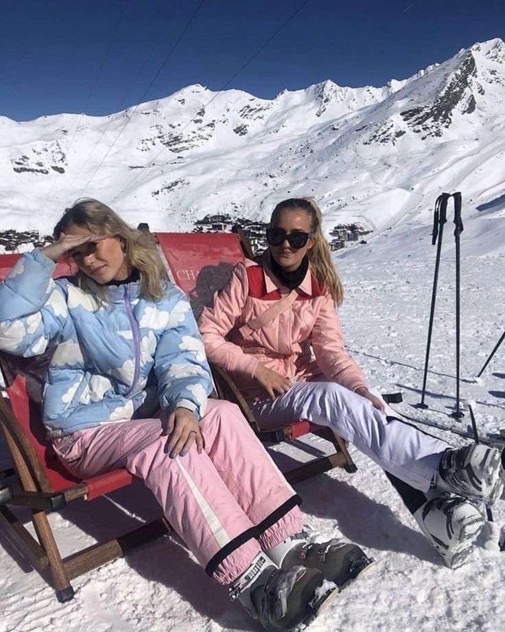 two people sitting on chairs in the snow with skis and poles behind their backs