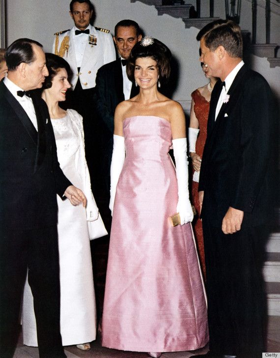 an old photo of two women in formal wear talking to three men and one woman