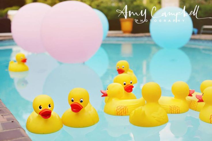 several rubber ducks sitting on the edge of a swimming pool with balloons in the background