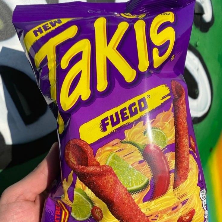 a hand holding a bag of faki's fuggie chips in front of a graffiti covered wall