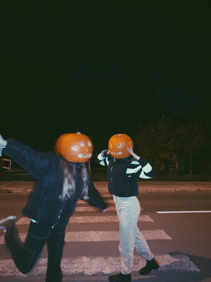 two people wearing orange helmets crossing the street at night with their arms in the air