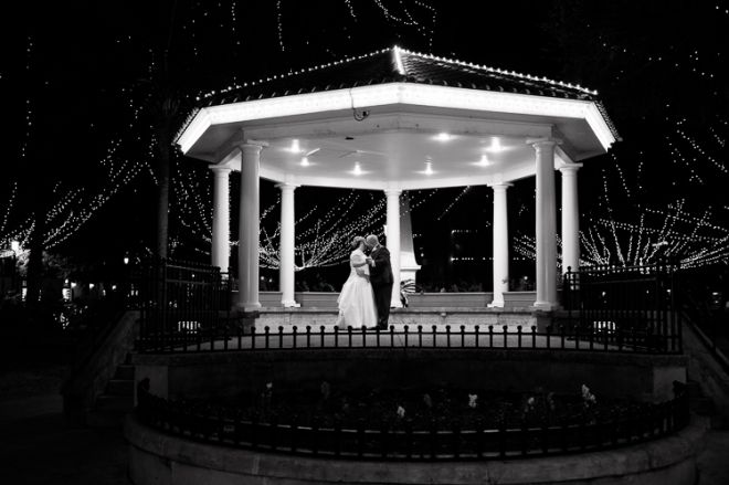 a bride and groom standing in front of a gazebo with christmas lights on it