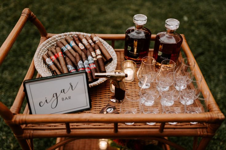 a wicker bar cart with cigars, liquor bottles and glasses sitting on it