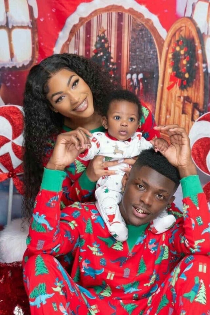 a man and woman in christmas pajamas holding a baby on their lap while posing for a photo