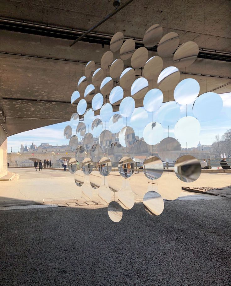 the reflection of people walking under an overpass with circular mirrors hanging from it's ceiling