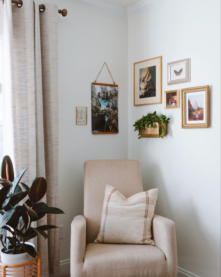 a living room with pictures on the wall and a chair next to a plant in a vase