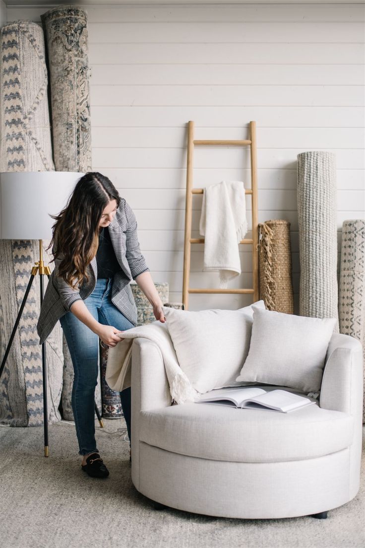 a woman sitting on top of a white couch next to a chair and rugs