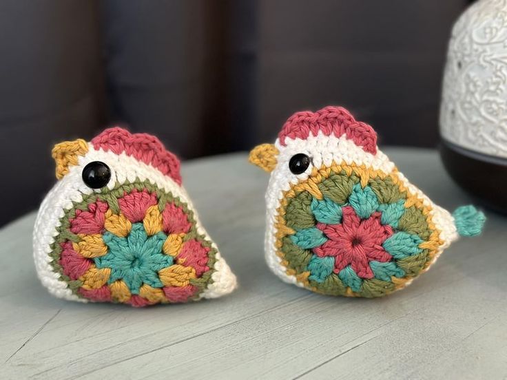 two small crocheted birds sitting on top of a table next to each other