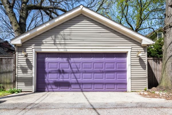 a purple garage door sits in front of a gray house with trees and grass around it