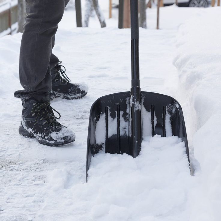 a person standing next to a shovel in the snow with it's front end covered by snow