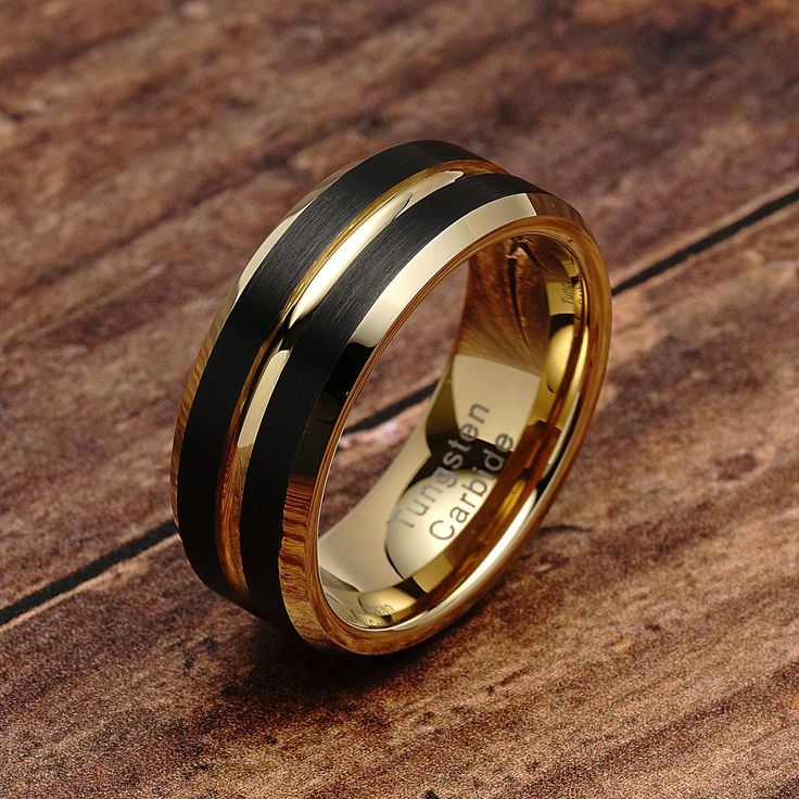 a gold and black wedding ring on top of a wooden table with wood inlays