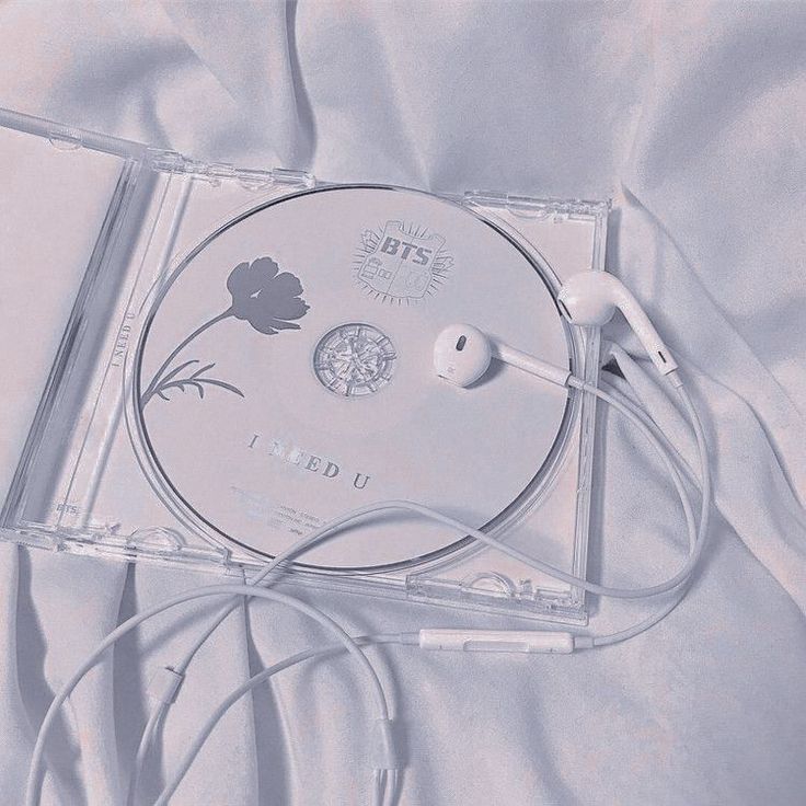 a cd case sitting on top of a bed covered in white sheets and headphones