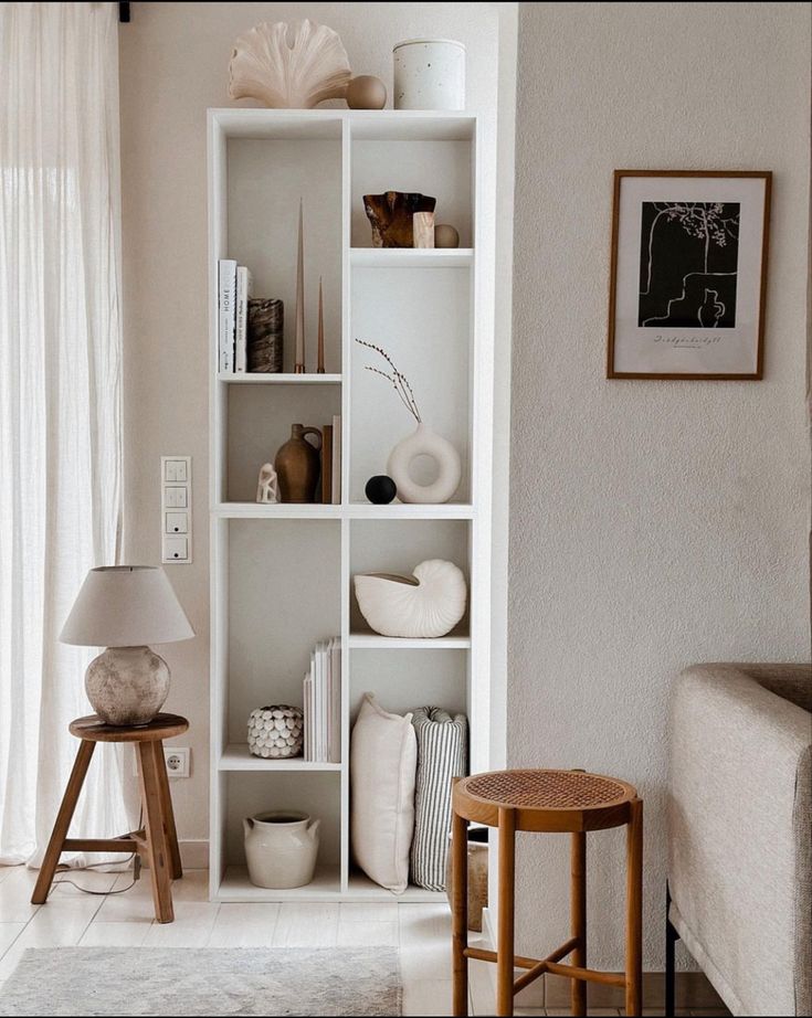 a living room filled with lots of furniture next to a white wall mounted shelf covered in vases and flowers