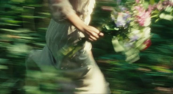 a blurry image of a woman holding flowers in her hands and walking through the woods