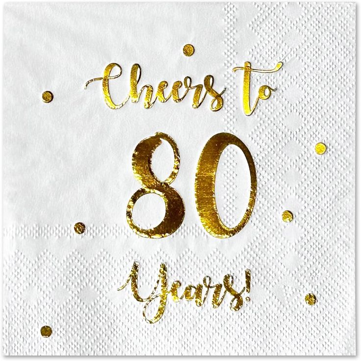 a white napkin with gold foil lettering that says cheers to 80 years