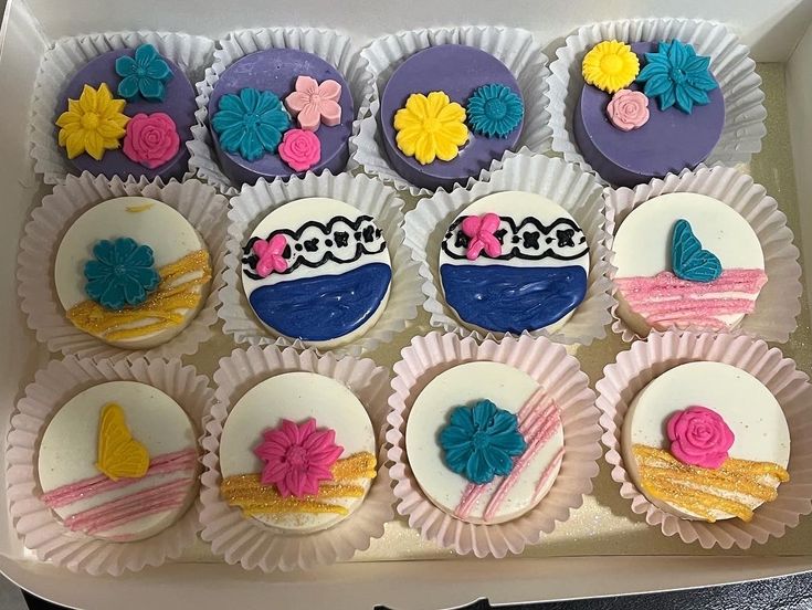 cupcakes decorated with colorful frosting and flowers in a white box on a table