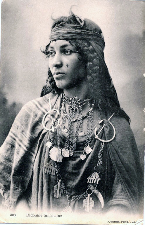 an old black and white photo of a woman with jewelry on her neck, wearing a headdress