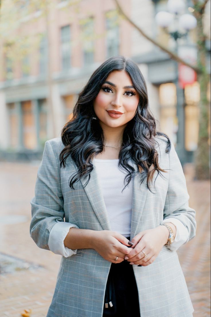 a woman standing in front of a building wearing a gray blazer and black pants