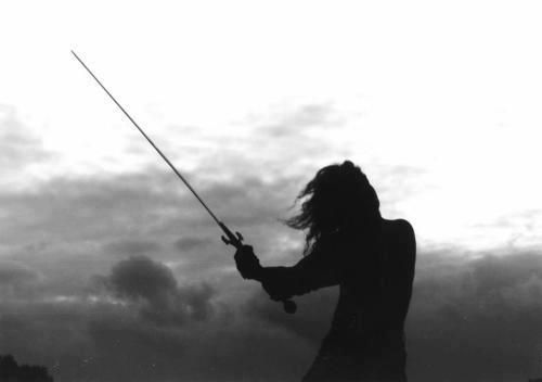 a woman holding a fishing pole while standing on top of a beach next to the ocean