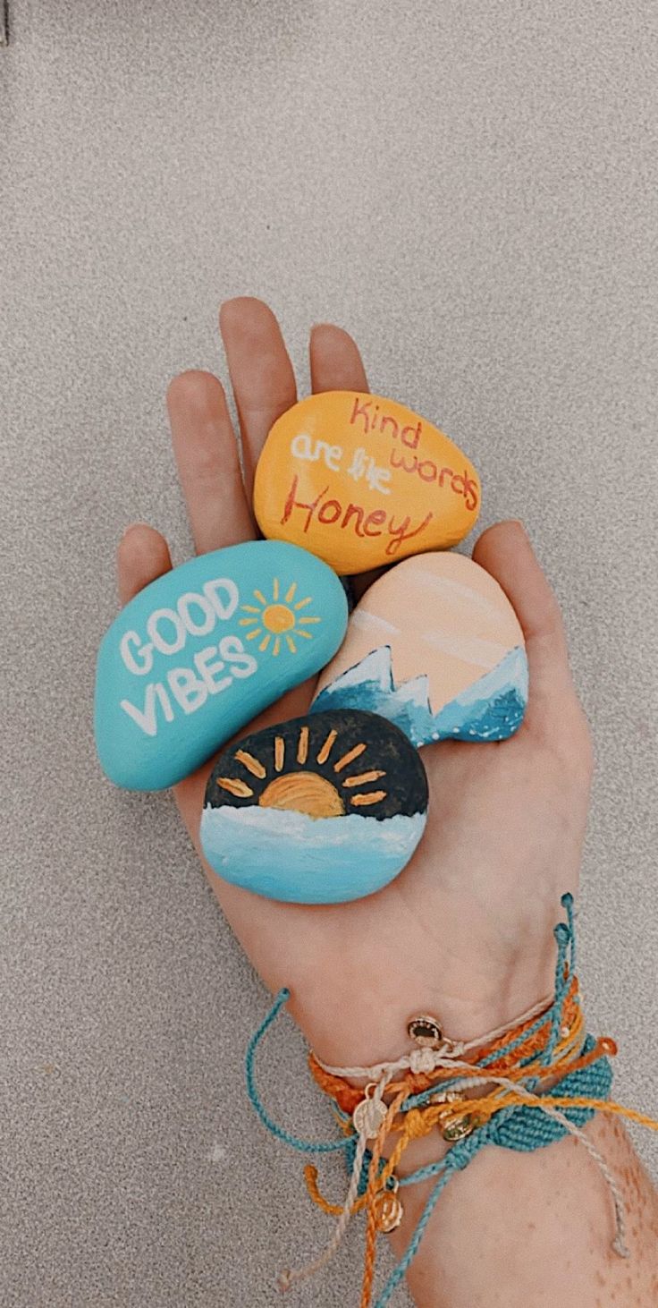 a hand holding three painted rocks that say good vibes