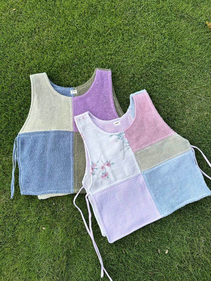 two vests laying on the grass next to each other with different colors and patterns