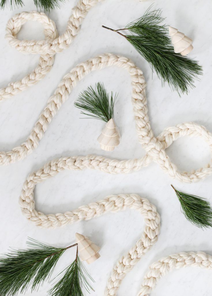 white rope with pine needles and cones attached to it on a marble surface, surrounded by evergreen leaves