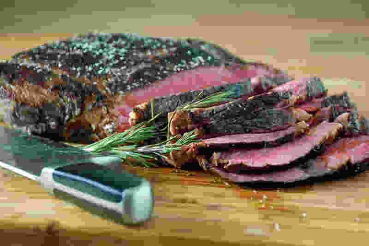 sliced meat on a cutting board next to a knife and pepper flaked sprig