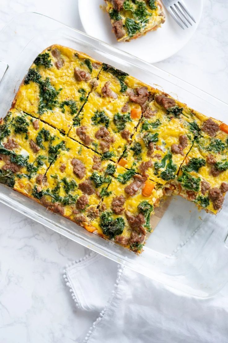 a casserole with meat, cheese and spinach in a glass dish on a marble table