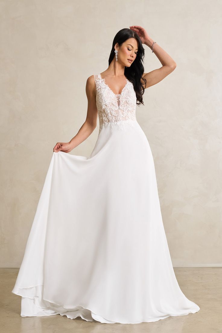 a woman in a white wedding dress posing with her hands on her head and looking at the camera