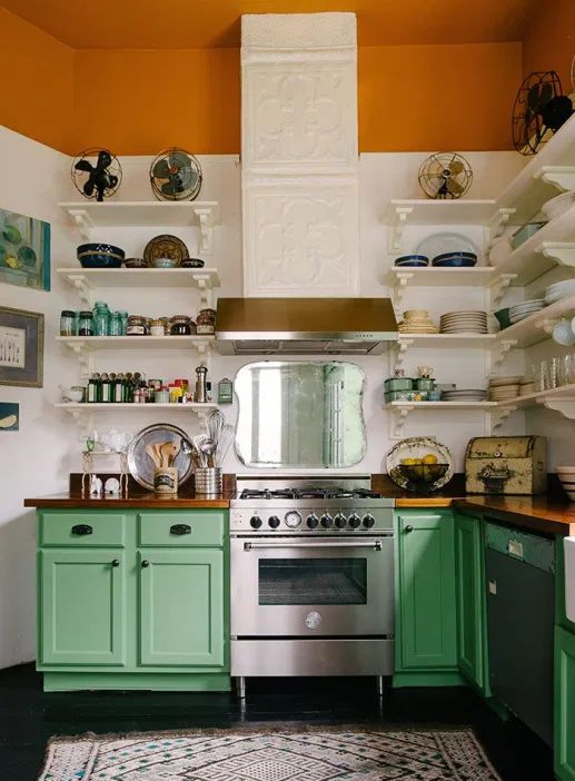 a kitchen with green cabinets and an oven in the center, surrounded by shelves filled with dishes