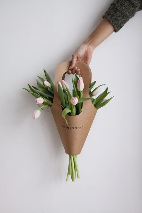 a person holding a bouquet of tulips in a brown paper bag on a white wall