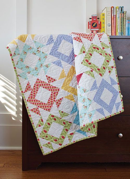 two quilts sitting on top of a dresser next to a bookcase with books