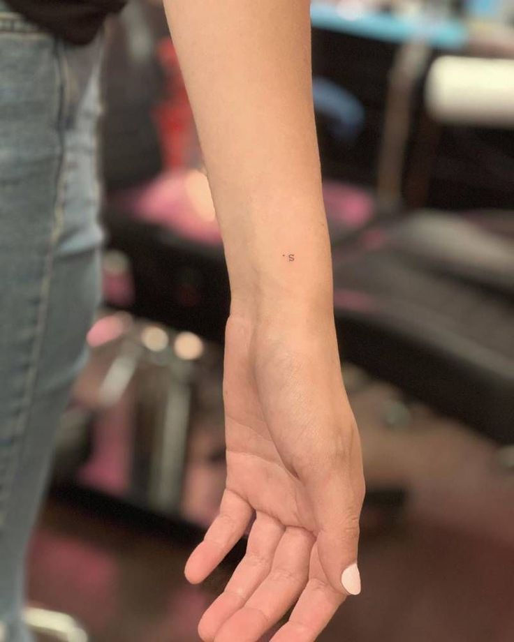 a woman's hand with a tiny tattoo on her left wrist, in front of a chair