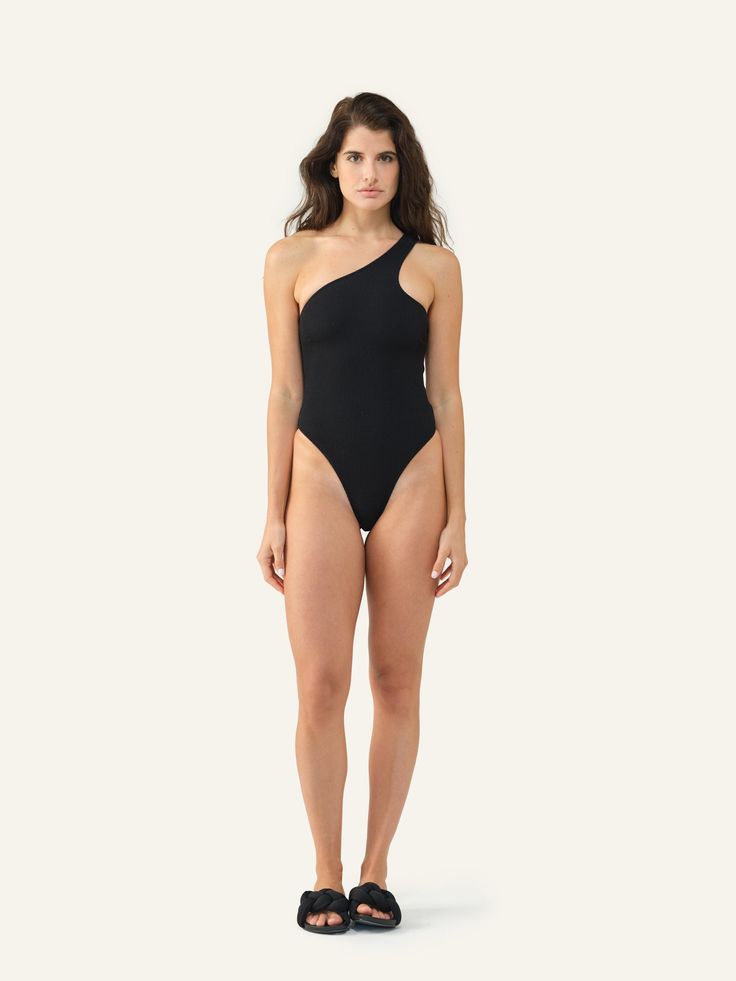 Meet Margot. With its striking asymmetrical neckline and high-cut leg silhouette, this one-piece swimsuit makes a bold statement. Black One-shoulder Stretch Swimwear, Black Fitted Bodysuit With Asymmetrical Neckline, Chic One-shoulder Bodysuit For Poolside, Chic High-cut Leg Swimwear, Modern Black Swimwear For Party, Black One-shoulder Bodysuit For Poolside, Chic One Shoulder Bodysuit For Swimming, Black One-shoulder Bodysuit For Swimming, Black One-shoulder Beachwear Bodysuit