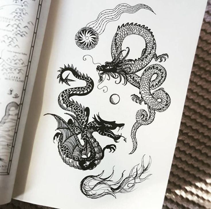 an open book with black ink drawings on it and a drawing of a dragon in the middle