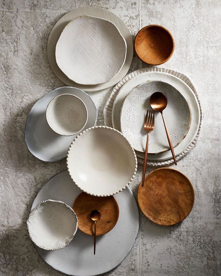 a table topped with white plates and silverware next to wooden spoons on top of each other