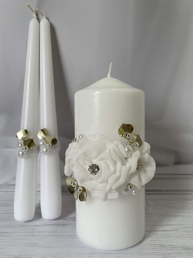 two white candles with flowers and pearls on them, next to the candle set for wedding