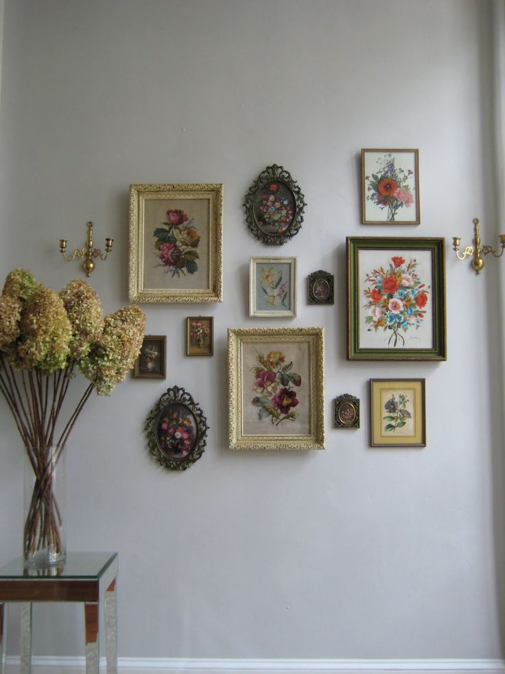 there are many framed pictures on the wall with flowers in vases next to it