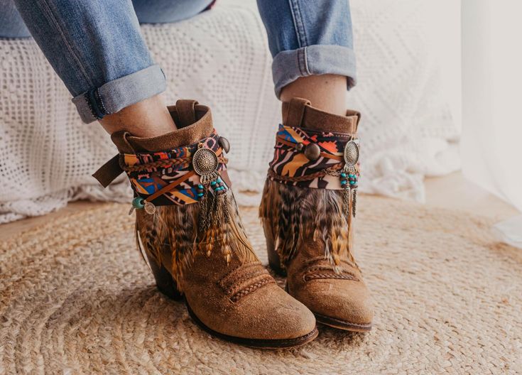 Step into the essence of Western charm with our handcrafted boot covers. Featuring a handmade suede braid and strip adorned with ancient Indian coins and natural khaki hair appliqué, topped with a central dream catcher in old gold. Embrace the spirit of the frontier with these unique and stylish boot accessories, perfect for adding a touch of rustic elegance to any ensemble. SPECIFICATIONS * Tribal boot covers * Made with multicolor ethnic printed scarf base and strip of feathers in beige tones Bohemian Brown Suede Boots, Bohemian Moto Boots With Round Toe For Fall, Bohemian Winter Suede Boots, Bohemian Suede Winter Boots, Multicolor Western Festival Boots, Bohemian Moto Boots For Festival In Fall, Multicolor Western Boots For Festivals, Bohemian Brown Winter Boots, Bohemian Leather Boots For Winter