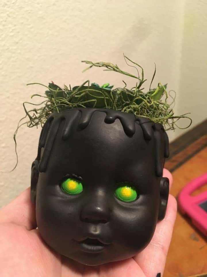 a hand is holding a black doll with green eyes and grass in it's head