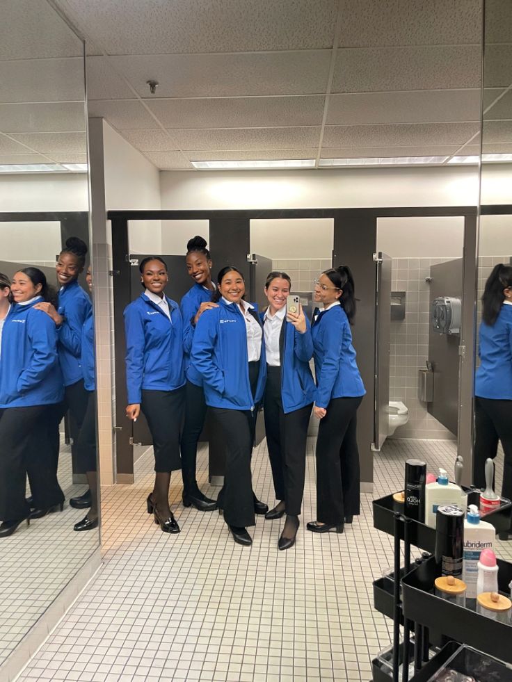 a group of women in blue jackets standing in front of a mirror with their arms around each other