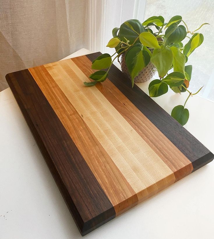 a wooden cutting board sitting on top of a table next to a potted plant