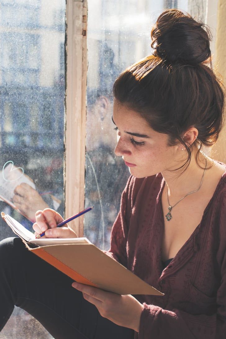 a woman sitting on the window sill writing with a pen and paper in her hand