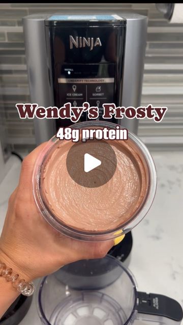 a person is holding up a chocolate frosting in front of a blender with the words wendy's frosty on it