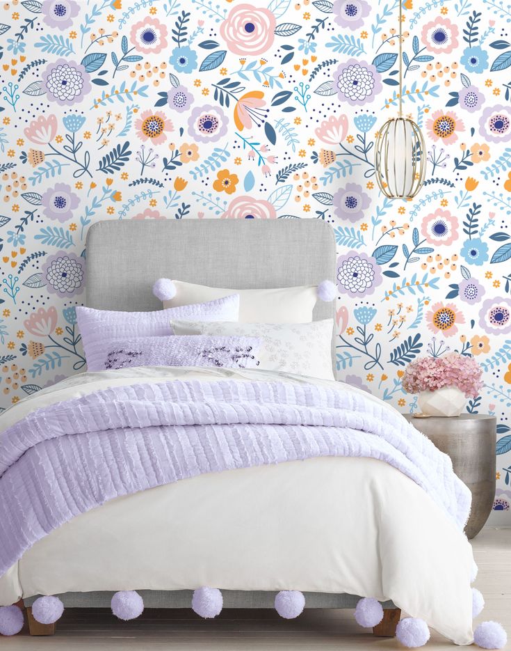 a bed with purple pom poms in front of a colorful floral wallpaper