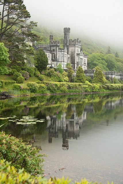 a large castle sitting on top of a lush green hillside next to a lake with lily pads