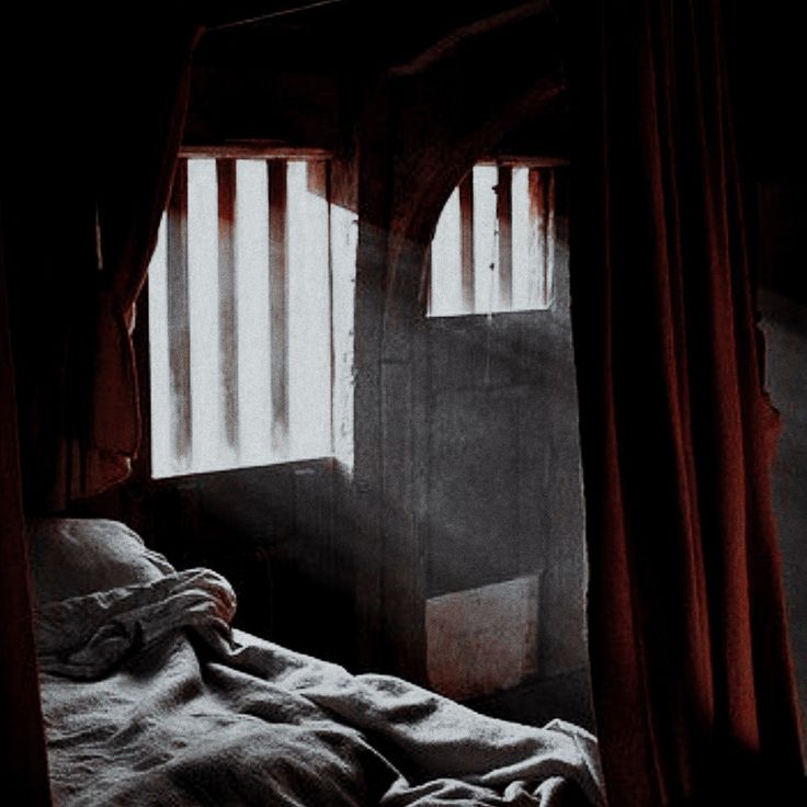 an unmade bed in a dark room with curtains