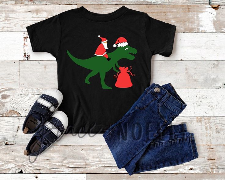 a t - shirt with a dinosaur and santa hat on it next to some jeans