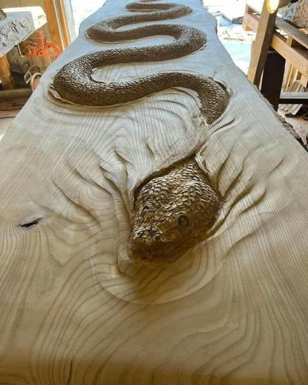 a large snake laying on top of a wooden table next to a bed with pillows